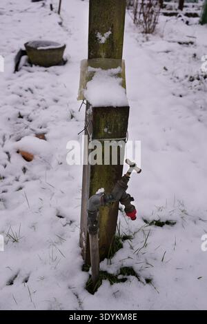 Ein Außenhahn oder Wasserhahn auf einem mit Schnee und Eis bedeckten Kleingut Stockfoto