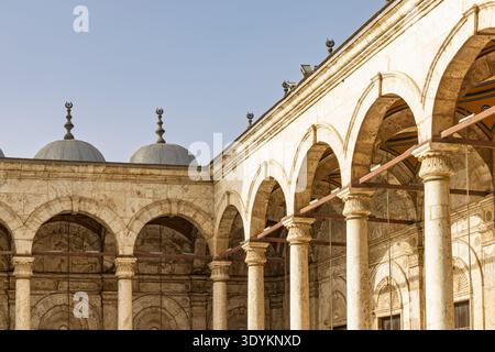 Historischer Moscheen-Innenhof in Kairo, Ägypten, mit verwitterten Steinbögen, geschnitzten Säulen und Kuppeln, die in warmes Sonnenlicht getaucht sind und an Geschichte und Ruhe erinnern Stockfoto
