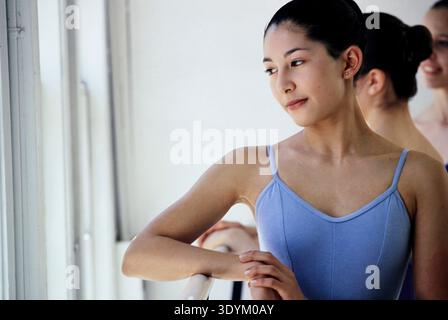 Eine junge weibliche Ballerina steht nachdenklich in einem Tanzstudio in der Nähe großer Fenster. Sie konzentriert sich auf ihre Bewegungen und bereitet sich auf einen Kurs vor. Die Stockfoto
