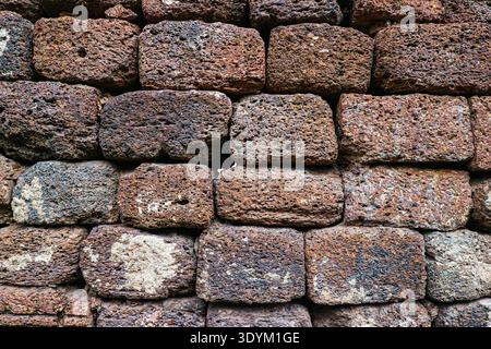 Alte Lateritsteinmauer mit verwitterter roter Textur. Antiker, gestapelter Mauerwerkhintergrund für historische und architektonische Tapeten. Stockfoto
