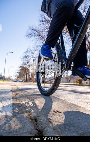 Person auf einem Fahrrad, die sich darauf vorbereitet, in die Pedale zu treten, sonniger Tag auf einer Stadtstraße, der aktiven Lebensstil und nachhaltige Verkehrsmittel einfängt Stockfoto
