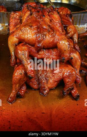 Nahaufnahme glasierter, gerösteter Hühner in einem lebhaften thailändischen Straßenrestaurant, in dem karamelisierte Haut und Marktküche hervorgehoben werden. Stockfoto