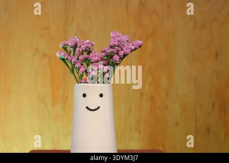 Smiley Vase mit rosafarbenen Blumen auf warmem orangefarbenen Hintergrund. Minimalistische Einrichtung mit positiver Stimmung und Kopierraum. Stockfoto