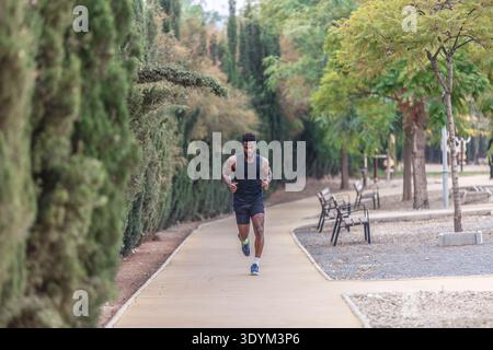 Voller Körper junger ethnischer Sportler in Sportbekleidung und Turnschuhen, die am sonnigen Herbstmorgen während des Workouts im Freien im Park laufen, während sie nach unten blicken Stockfoto
