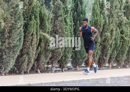 Voller Körper eines entschlossenen schwarzen männlichen Athleten in Turnschuhen und Sportbekleidung, der während des Cardio-Outdoor-Fitness-Trainings am Sommerwochenende im Park läuft Stockfoto