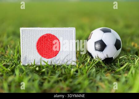 Japanische Flagge und Fußball auf sonnendurchflutetem Stadiongras. Profisport-Hintergrund für Nachrichten über internationale Fußballwettbewerbe. Stockfoto