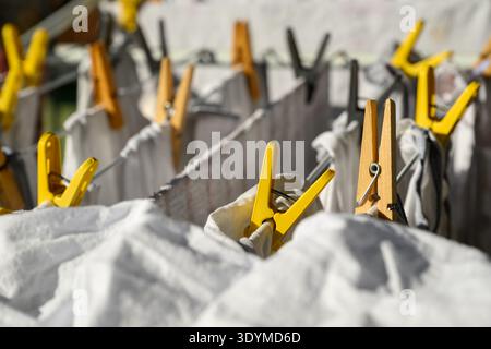 Nahaufnahme von frisch gewaschenen weißen Bettlaken und Bettwäsche, die an einer mit Kleiderschränken versehenen Wäscheleine hängen, selektiv fokussiert. Stockfoto