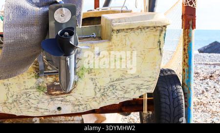 Nahansicht des abgenutzten Außenbordmotors und Propellers, die am verblassten Bootsrumpf befestigt sind (74 Zeichen) Stockfoto