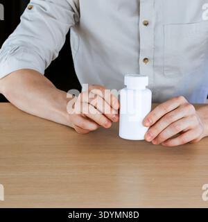 Männliche Hände greifen eine weiße Plastikpille aufrecht auf einem glatten Holztisch Stockfoto