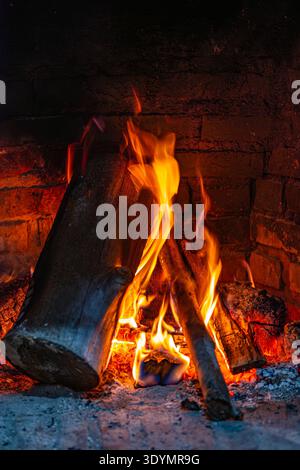 Nahaufnahme von leuchtend orange und gelben Flammen, die hell um Holzscheite in einem rustikalen Ziegelkamin brennen. Stockfoto