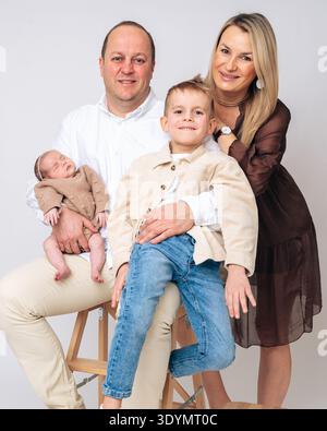 Glückliche Eltern sitzen zusammen mit ihren Kindern neugeborenes Baby und älterer Junge. Herzliches Familienporträt, das Liebe, Erziehung und emotionale Bindung zeigt Stockfoto