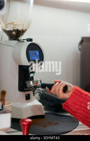 Barista im Strickpullover, der die Kaffeemühle für die Verarbeitung von Bohnen im Geschäft einrichtet Stockfoto