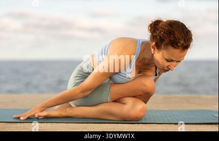 Ardha Matsyendrasana Yoga Pose - Frau, die Yoga am Strand macht Stockfoto