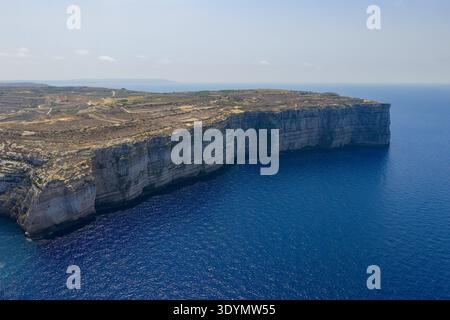 Blick aus der Vogelperspektive auf zerklüftete Kalksteinklippen und felsiges Plateau über ruhigem tiefblauem Mittelmeer in der Dwejra Bay, Gozo. Stockfoto