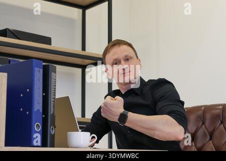 Der aufgeregte Mann in Geschäftskleidung feiert Erfolge mit erhobener geballter Hand in der Nähe des Computerbildschirms Stockfoto
