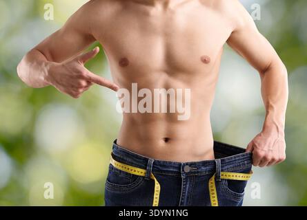 Mann, der auf seine alte Jeans vor verschwommenem grünem Hintergrund zeigt, Nahaufnahme. Gewichtsverlust Stockfoto