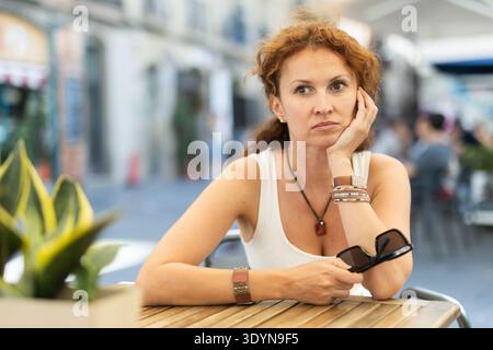 Nachdenkliche Frau mittleren Alters, die im Open-Air-Café sitzt Stockfoto