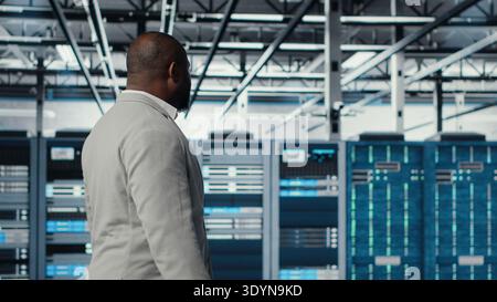 Systemadministratoren laufen im Rechenzentrum mit Rigs, die Abfragen bearbeiten und Sicherungen durchführen. Verwaltung der Serverfarm mit Ausrüstung, die digitale Dienste hostet, Client-Plattformen unterstützt, Kamera B Stockfoto