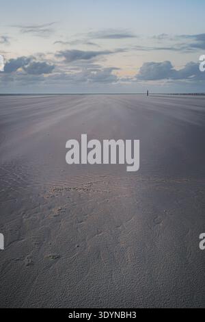 Der weite Sandstrand in Ameland erstreckt sich endlos unter einem weichen, bewölkten Himmel. Sanfte Windmuster erzeugen subtile Texturen über den kühlen, mutigen Himmel Stockfoto