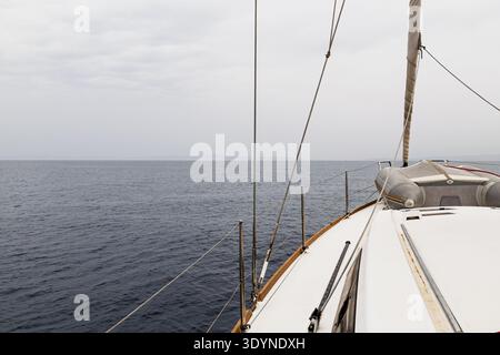 Ein nach vorne gerichteter Blick vom Deck eines Segelbootes, das auf ruhigem offenem Wasser navigiert. Stockfoto