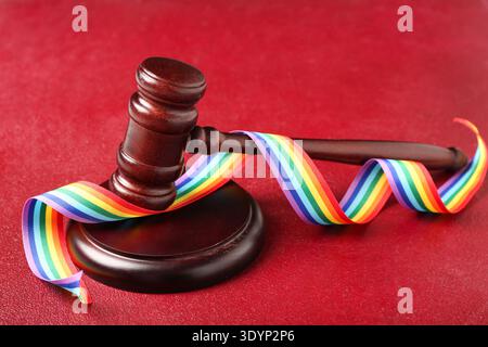 Richterlicher Hammer mit Regenbogenband auf rotem Hintergrund. LGBT-Konzept Stockfoto
