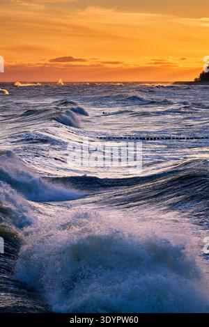 Während eines Wintersturms krachen mächtige Wellen entlang der Ostseeküste von Koserow, Deutschland, die in den leuchtenden Orange- und Goldtönen eines frühen M getaucht sind Stockfoto