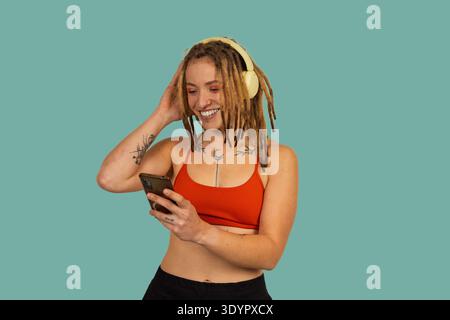 Junge Frau mit Dreadlocks lächelt, hört Musik über Kopfhörer und hält ein Smartphone Stockfoto