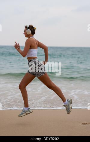Sportliche Lauffrau. Aktive Sportlerin In Stilvollem Outfit, Die Am Frühen Morgen Über Den Strand Fährt Stockfoto
