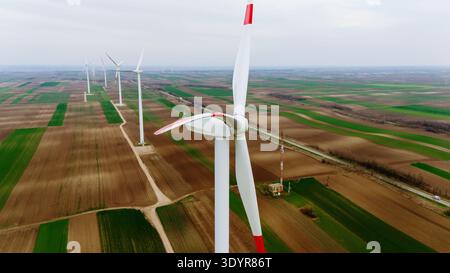 Aus der Vogelperspektive erhebt sich der Blick auf die hoch aufragenden Windturbinen, die sich als stille Wächter über dem riesigen Flickenteppich von Feldern, einer Mischung aus Erdbraun und lebhaftem Grün, erheben Stockfoto