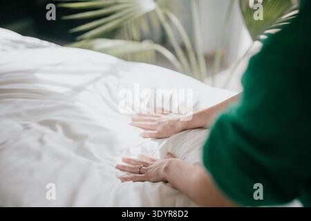 Die Person berührt sanft das weiße Bettlaken. Grüne Ärmel sorgen für Ruhe. Sanftes Licht sorgt für eine gemütliche Morgenatmosphäre. Perfekt für Wellness, Schlaf oder Relaxati Stockfoto