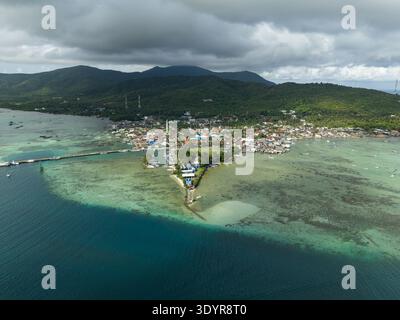 Blick aus der Vogelperspektive auf den pulsierenden Stadtplatz, der auf das ruhige türkisfarbene Meer trifft, im Kontrast zu den üppigen grünen Hügeln unter einem bewölkten Himmel, Karimunjawa, Cent Stockfoto
