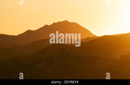 Blick auf das warme Sonnenlicht, das lange Schatten über eine zerklüftete Bergkette wirft und die trockene Landschaft mit einem goldenen Schein beleuchtet, Brandberg, Erongo Regio Stockfoto