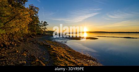 Goldener Sonnenuntergang über ruhigen Küstengewässern und Rocky Shoreline Stockfoto