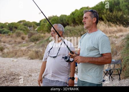 Zwei Männer fischen und reden am felsigen Strand Stockfoto