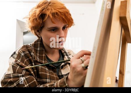 Malerin, die im Atelier mit Pinsel auf Leinwand arbeitet. Stockfoto