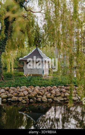 Entenhaus auf einer kleinen Insel unter Weiden im Park Teich Stockfoto