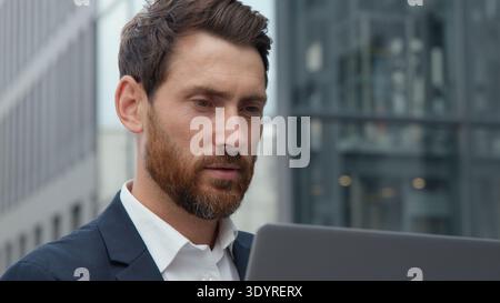 Nahaufnahme fokussierter nachdenklicher kaukasischer Geschäftsmann aus den 40er Jahren, der auf Laptop-Bildschirm schaut professioneller reifer denkender Geschäftsmann, der mit Computer in der Stadt arbeitet Stockfoto