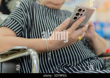 Nahhände einer älteren Frau im Rollstuhl mit Handy. Alderly Senior mit Smartphone. Selektiver Fokus. Stockfoto