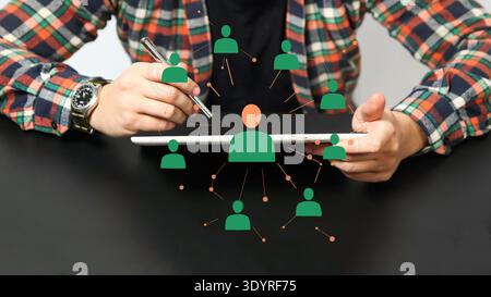Konzept des sozialen Netzes und der Humanressourcen. Mann, der ein digitales Tablet mit fliegenden Avatarsymbolen für Netzwerke, Rekrutierung und Teammanagement verwendet. HR-Konz Stockfoto
