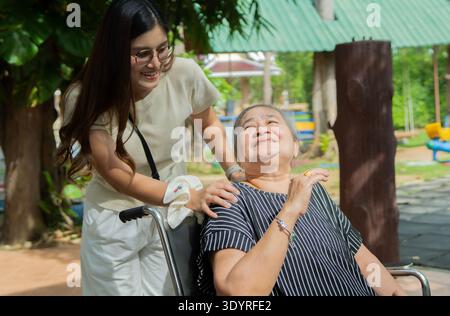 Glückliche asiatische Seniorengroßmutter und Kindermädchen, die sich im Park entspannen. Lächelnde ältere Frau im Rollstuhl mit Enkelin, die Spaß hat und mich redet Stockfoto