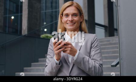 Zufriedene weiße Geschäftsfrau mittleren Alters mit Mobiltelefon lächelnd Blick in die Kamera glückliche Erwachsene Geschäftsfrau Porträt mit Smartphone Stockfoto