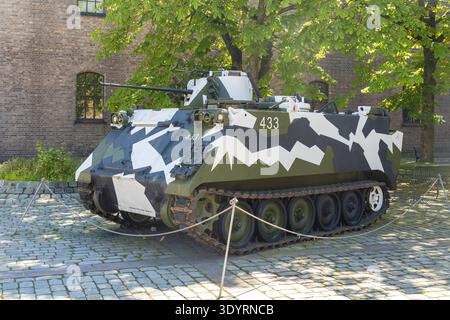 Der Blick auf einen Militärpanzer mit Tarnmuster befindet sich deutlich auf einer Kopfsteinoberfläche in der Nähe eines alten Backsteingebäudes in Oslo, Oslo, Norwegen. Stockfoto