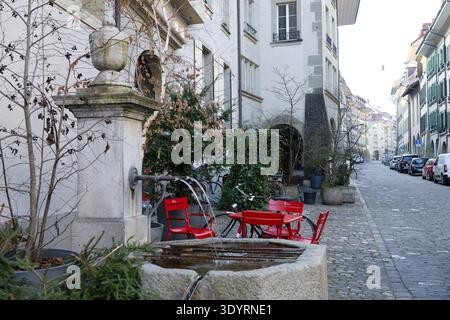 Charmante Straße in Bern, Schweiz mit traditionellem Brunnen und roten Stühlen auf Kopfsteinpflasterstraße. Stockfoto