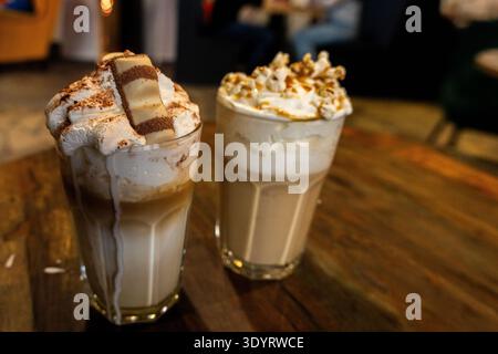 Ein Editorial-Bild von zwei verschiedenen Gourmet-Eiskaffee-Drinks, die nebeneinander auf einem Holztisch in einem Café serviert werden. Einer ist mit Schlagsahne und einem belegt Stockfoto