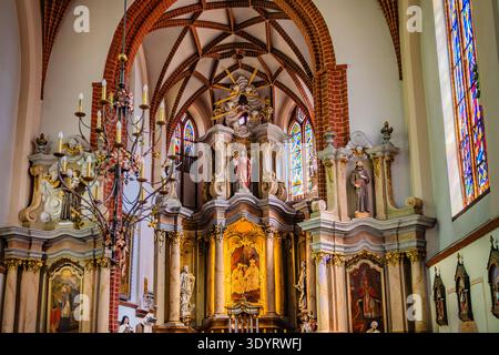 Nahaufnahme der kunstvollen barocken Altardekoration und der lebendigen Buntglasfenster in der historischen St. Annenkirche in Vilnius. Stockfoto