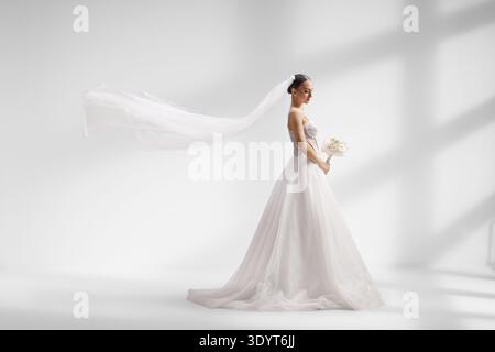Braut in einem weißen Hochzeitskleid mit einem langen wehenden Schleier und Schatten auf einer Wand als Hintergrund Stockfoto