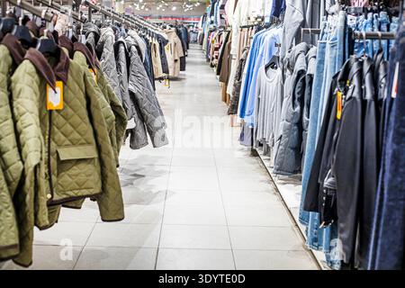Moderne Unisex-Jacken, -Westen und -Cardigans an Kleiderbügeln in der Bekleidungsabteilung Stockfoto