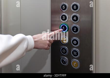 Drücken Sie Von Hand Auf Die Lifttaste Im Ersten Stock. Nahaufnahme einer Frau, die den Knopf im ersten Stock in einem Aufzug drückt, mit modernen Aufzugsteuerungen Stockfoto