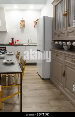 Saubere Küche mit Esstisch, modernem, weißem Kühlschrank, traditionellem Holzschrank und gefliesten Wänden Stockfoto