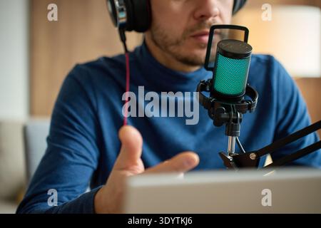Mann mit Kopfhörern, die in das Mikrofon am Arm vor dem Laptop sprechen. Konzept für Podcast-Aufnahme, Online-Streaming und Audio-conte Stockfoto